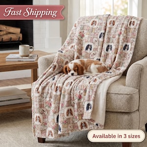 Könnte beinhalten: Eine weiche Wohndecke mit einem wiederkehrenden Muster aus Cavalier King Charles Spaniel Hunden und Blumenmotiven in Beige-, Rosa- und Brauntönen. Die Decke hat eine weiche, strukturierte Oberfläche und liegt über einem neutralen Sessel.