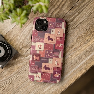 May include: A phone case with a patchwork design featuring various corgi illustrations in shades of pink, red, and cream. The case has a glossy finish and a camera cutout. The background is a wooden surface.