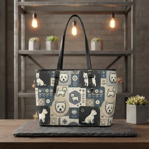 Könnte beinhalten: Eine Tragetasche mit einem Patchwork-Muster aus West Highland White Terriern in verschiedenen Posen, durchsetzt mit Blumenmotiven in Creme-, Beige- und Schieferblautönen. Die Tasche hat zwei schwarze Leder-Schulterriemen mit Metallschnallen.