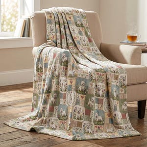 May include: A woven throw blanket featuring a repeating patchwork pattern of white West Highland White Terrier dogs, colorful floral arrangements, and small red hearts in muted tones of green, blue, tan, and cream draped over a beige armchair.