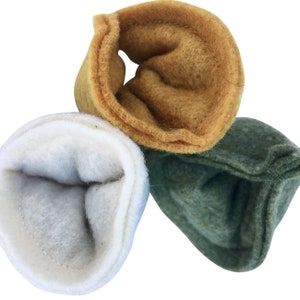 May include: Three felted wool items in shades of white, gold, and green. The items are folded over, revealing a contrasting interior. The textures appear soft and the colors are muted, suggesting a natural or handmade origin.