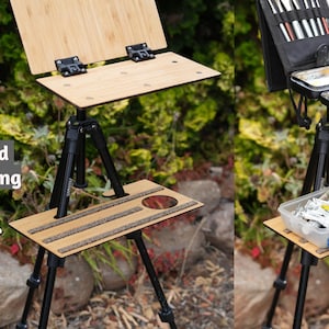 May include: A wooden easel with a tripod stand and a shelf for supplies. The easel is set up outdoors on a grassy surface. The shelf is sold separately.