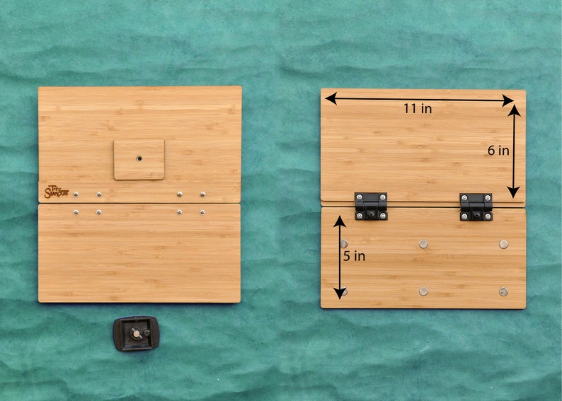 May include: A bamboo folding table with two hinges and a small square cutout in the top panel. The table is 11 inches wide, 6 inches deep, and 5 inches tall when folded. The table is made of natural bamboo and has a light brown color.