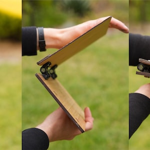 May include: A wooden folding easel in three positions: fully open, partially open, and fully closed. The easel is made of light brown wood and has black metal hinges.