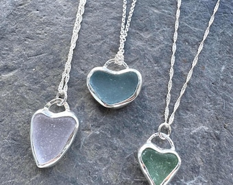 Può includere: Tre collane con pendenti a forma di cuore realizzati in vetro marino liscio e satinato nelle tonalità lavanda, verde acqua e verde. Ogni pendente è racchiuso in una cornice di metallo color argento lucido e pende da una sottile catena intrecciata.