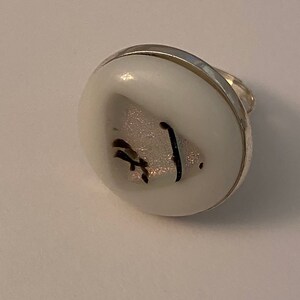 May include: A white ring with a silver band and a white glass cabochon with a black and silver design.
