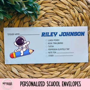 May include: A light blue personalized school envelope with the name "Riley Johnson" in blue. It features an astronaut riding a blue pencil. The envelope includes sections for lunch money, book fair, tuition, and permission slips.