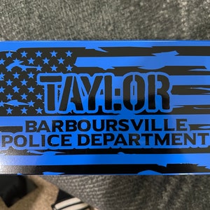 May include: A blue and black sign with a distressed American flag design. The text "TAYLOR BARBOURSVILLE POLICE DEPARTMENT" is printed in black.
