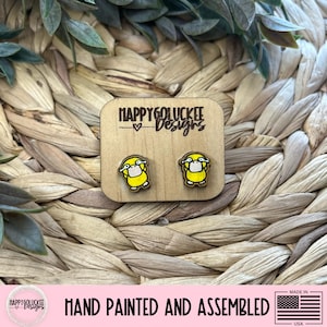 May include: Wooden stud earrings featuring a yellow cartoon duck wearing a white face mask. The earrings are hand-painted and assembled. The earrings are on a wooden display card with the text "HAPPYGOLUCKEE Designs".