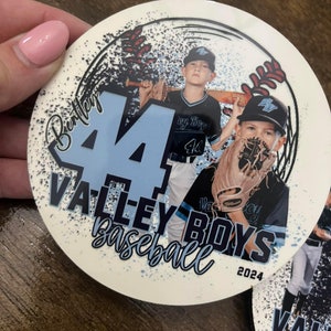 May include: A white round sticker with a baseball theme. It features two boys in baseball uniforms, one holding a bat and the other holding a glove. The sticker has a black and white splatter effect and the text "Bentley 4 Valley Boys Baseball 2024".