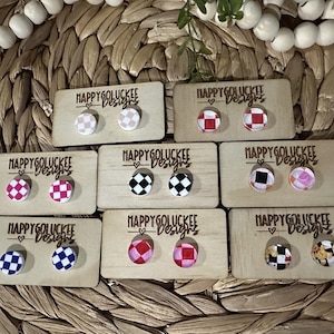 May include: Assortment of checkerboard patterned earrings on display cards. The cards are labeled "Happy Go Luckee Designs". The earrings are in various colors, including red, black, white, and pink.