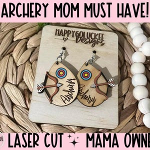 May include: A pair of wooden earrings shaped like an arrow with a target in the center. The earrings are laser cut and have the word "Archery" written on them. The earrings are displayed on a wooden board with the text "Happy Go Luckee Designs" and "Laser Cut Mama Owned".