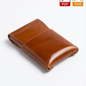 Op de afbeelding: Een bruine leren kaarthouder met een glanzende afwerking. De rechthoekige hoes heeft een gevouwen ontwerp en een contrasterende naad in een lichtere kleur. De afbeelding bevat ook PDF- en SVG-pictogrammen.