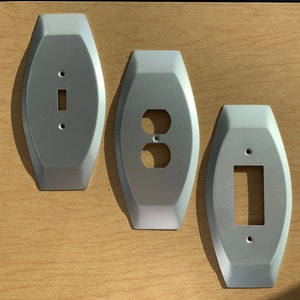 May include: Three silver metal wall plates with different cutouts. The plate on the left has a single switch cutout, the middle plate has a double outlet cutout, and the plate on the right has a single switch cutout.