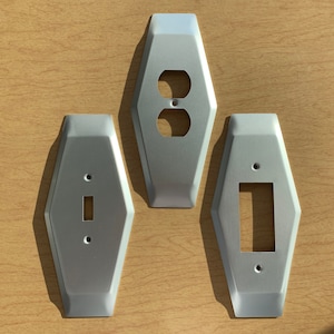 May include: Three silver metal wall plates with different cutouts for electrical outlets and switches. The plates are in a hexagonal shape with rounded edges.