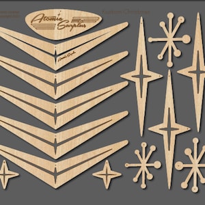 May include: Laser-cut wooden Christmas ornaments in a mid-century modern style. The set includes boomerang shapes, starbursts, and snowflakes. The text "Atomic Surplus" and "Kustom Christmas" are visible. The ornaments are made of light-colored wood.