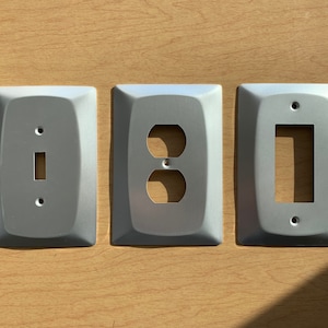 May include: Three silver wall plates with different electrical outlet and switch cutouts. The plates are rectangular and have rounded corners.