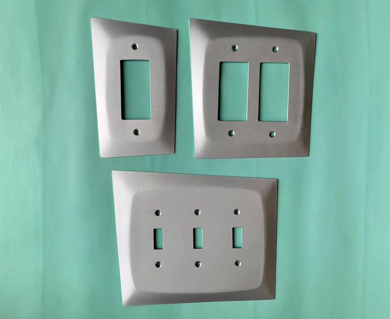 May include: Three silver metal light switch plates. The top plate has two switches, the middle plate has one switch, and the bottom plate has two switches.