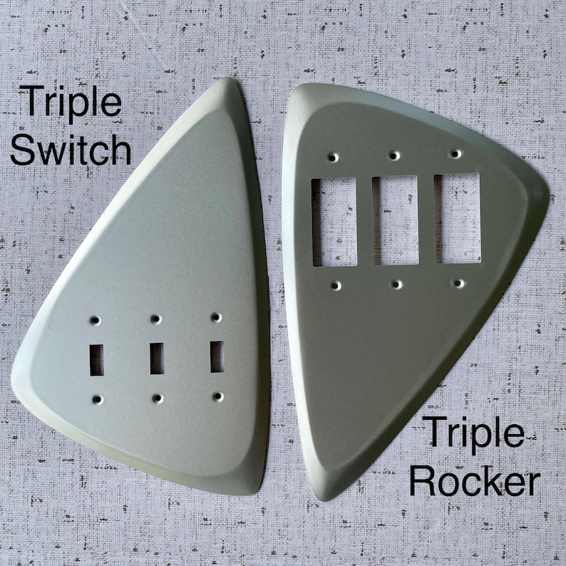 May include: Two silver-coloured, triangular-shaped wall plates. The left plate is labelled Triple Switch and features three small rectangular openings. The right plate is labelled Triple Rocker and features three larger rectangular openings.