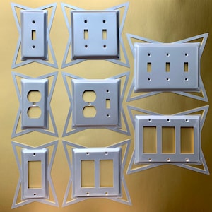May include: A set of eight white plastic electrical outlet covers in various configurations, including single, double, and triple switch plates, and a single outlet plate. The covers are arranged in a starburst pattern on a gold background.