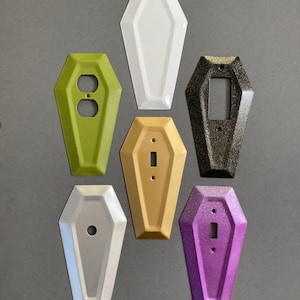 May include: Set of six coffin-shaped light switch covers in various colors, including white, green, gold, black, and purple.