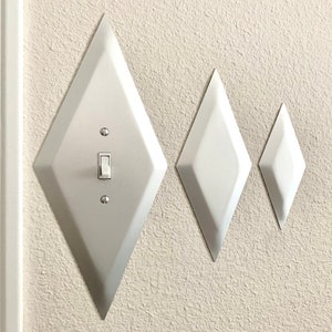 May include: Three white diamond-shaped light switch covers, the largest one has a light switch with a white toggle.