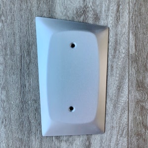 May include: A white, rectangular wall plate with rounded edges and two small holes. The plate is mounted on a wood-grain surface.