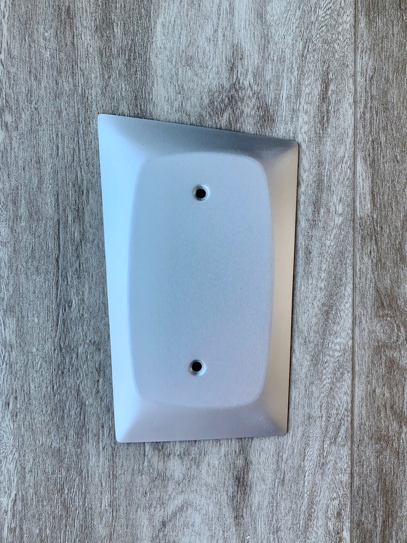 May include: A white, rectangular wall plate with rounded edges and two small holes. The plate is mounted on a wood-grain surface.