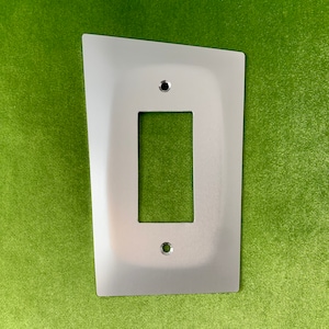 May include: A silver metal light switch plate with a rectangular opening for a light switch. The plate has rounded corners and two small screw holes.