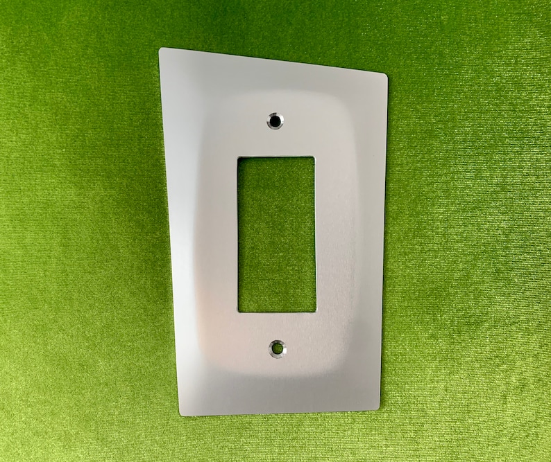 May include: A silver metal light switch plate with a rectangular opening for a light switch. The plate has rounded corners and two small screw holes.