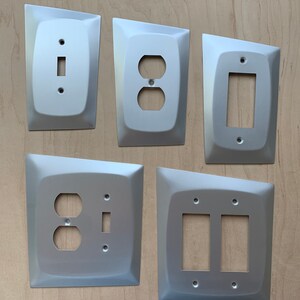 May include: Five silver wall plates with different electrical outlet and switch configurations. The plates have a modern, angular design.