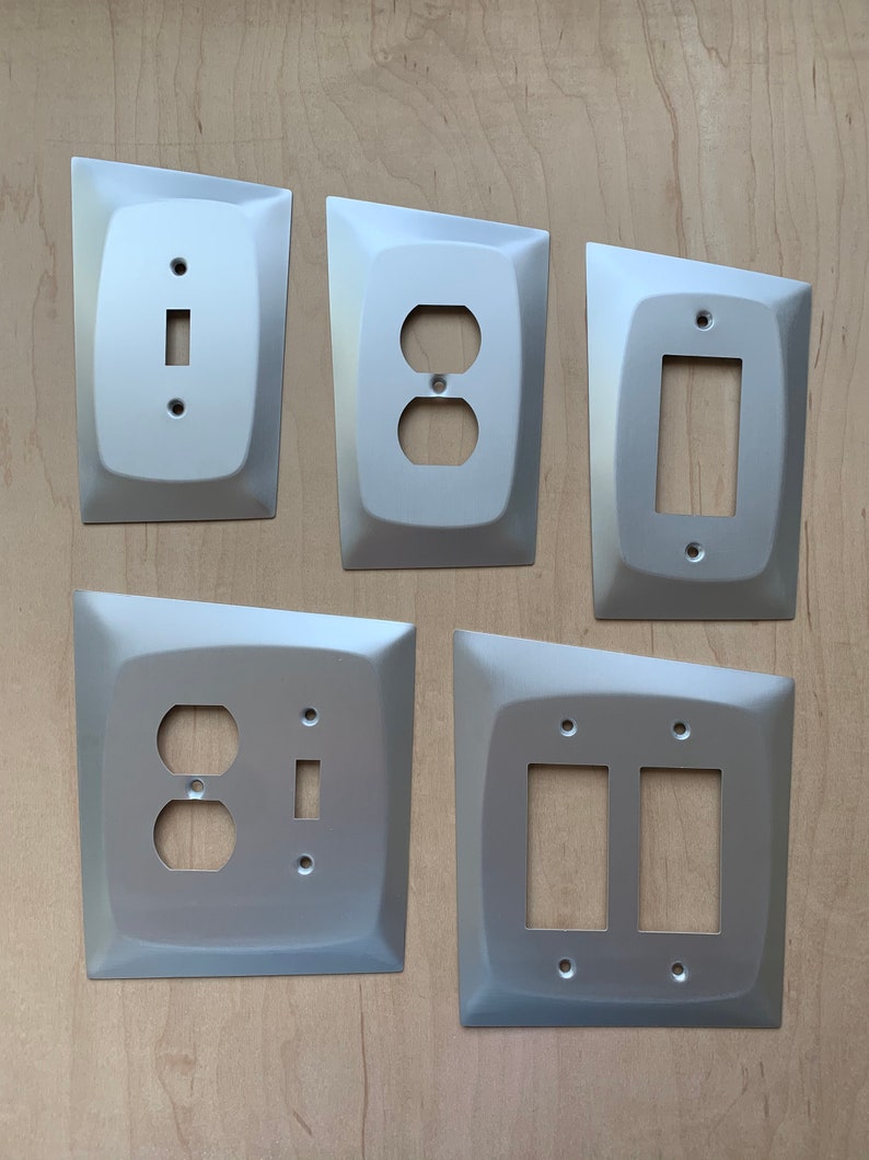 May include: Five silver wall plates with different electrical outlet and switch configurations. The plates have a modern, angular design.