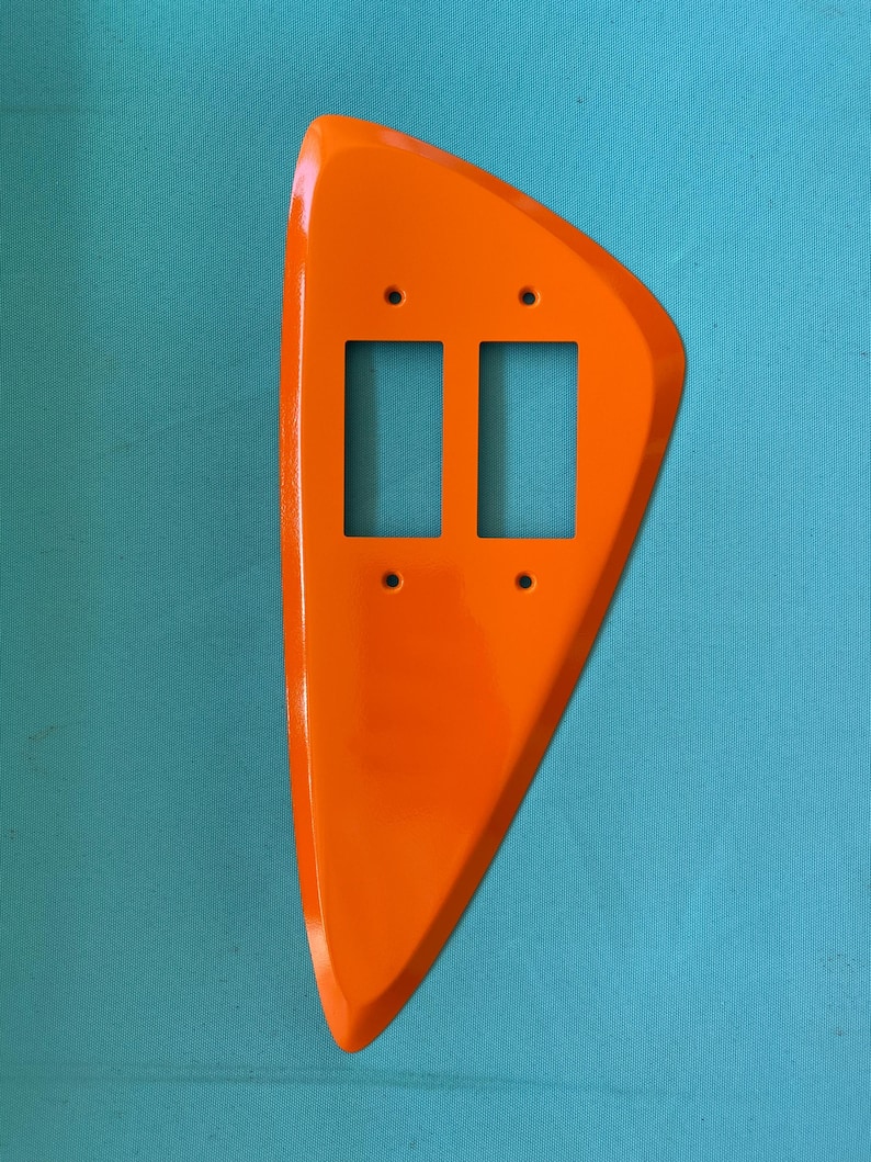 May include: A bright orange, asymmetrical wall plate cover featuring a smooth, glossy finish. This decorative switch plate is designed to accommodate two rectangular rocker-style light switches and includes four small circular screw holes.