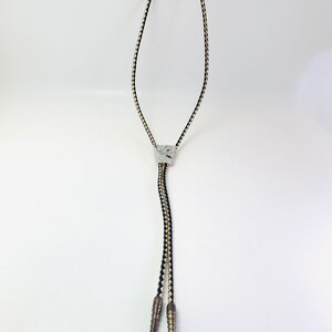 May include: A black and tan braided bolo tie with silver tips and a silver clasp.