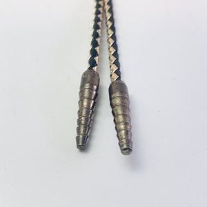 May include: Close-up of a black and white braided leather bolo tie with silver tips.