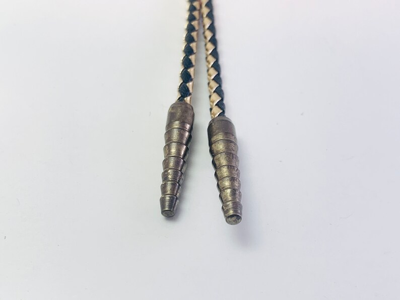 May include: Close-up of a black and white braided leather bolo tie with silver tips.
