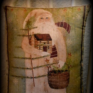 May include: Rectangular pillow with a vintage Santa Claus design. Santa is depicted in a white robe, holding a small log cabin and a basket of greenery. The background is a muted green with snowflakes and stars.