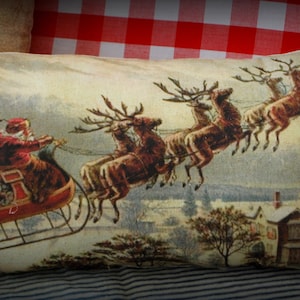 May include: A vintage-style Christmas pillow featuring a beige background with a red sleigh pulled by reindeer flying through a snowy landscape. Santa Claus is in the sleigh with a group of children.