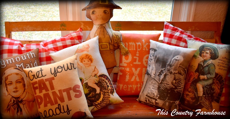 May include: A wooden bench with a variety of decorative pillows. The pillows feature Thanksgiving-themed designs, including turkeys, pilgrims, and the text "Get your fat pants ready" and "Pumpkin pie fixin' everyt".