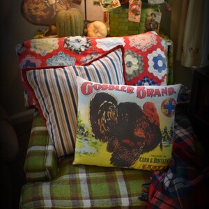 May include: A green plaid couch with red and white checkered throw pillows. The couch has a red and white checkered ottoman in front of it. The couch is decorated with a red, white, and blue quilt and a throw blanket with a plaid pattern. The couch is also decorated with a pillow with a turkey on it and the words "Gobbler Brand" printed on it.