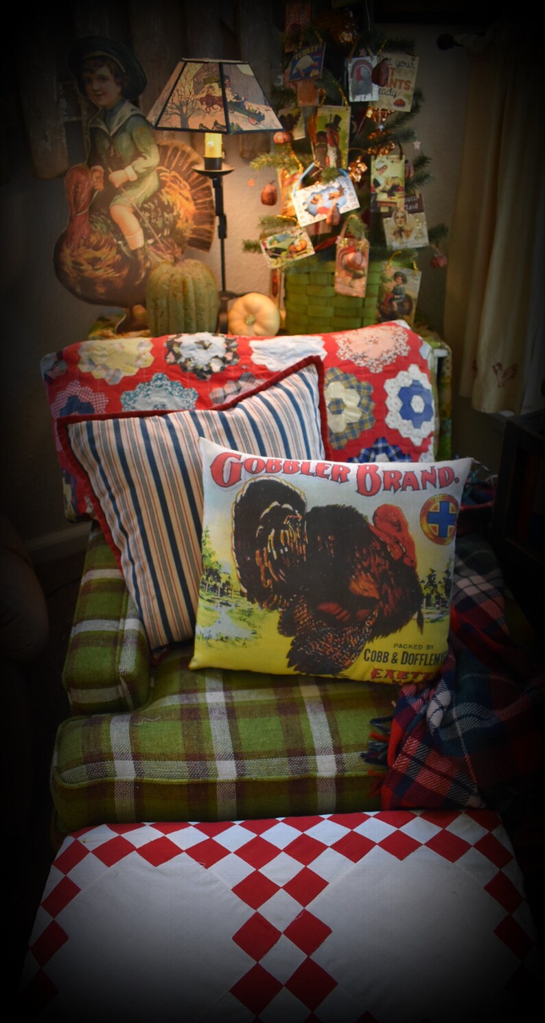 May include: A green plaid couch with red and white checkered throw pillows. The couch has a red and white checkered ottoman in front of it. The couch is decorated with a red, white, and blue quilt and a throw blanket with a plaid pattern. The couch is also decorated with a pillow with a turkey on it and the words "Gobbler Brand" printed on it.