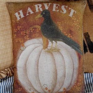 May include: A decorative throw pillow with a white pumpkin and a black bird on top. The pillow has a brown background with the word "HARVEST" printed in white.