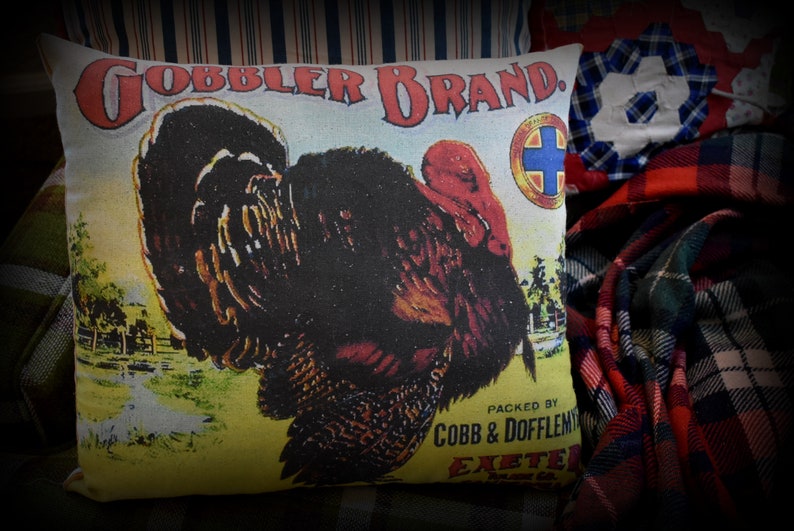 May include: A vintage-style pillow featuring a colorful illustration of a turkey with the text "GOBBLER BRAND. PACKED BY COBB & DOFFLEMYER EXETER, N.H."