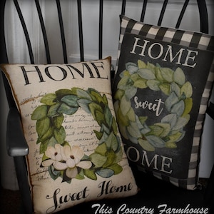May include: Two decorative throw pillows with a black and white checkered pattern and a cream background. The pillows feature a green wreath with white flowers and the text "HOME sweet HOME" and "HOME sweet OME".