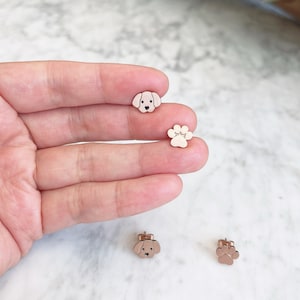 May include: A pair of gold-toned stud earrings featuring a dog head and a paw print design.