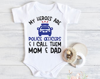 May include: White baby onesie with black text that reads "My heroes are police officers & I call them mom & dad". A blue police car graphic is above the text.