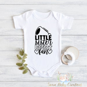 May include: White baby onesie with black text that reads "Little sister biggest fan" with two black hearts.