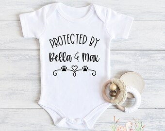 May include: White baby onesie with black text that reads "Protected by Bella & Max" with paw prints and a heart.
