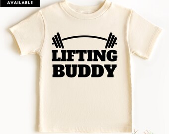 May include: A cream colored short-sleeved t-shirt with a black barbell and the text "Lifting Buddy" printed on the front.