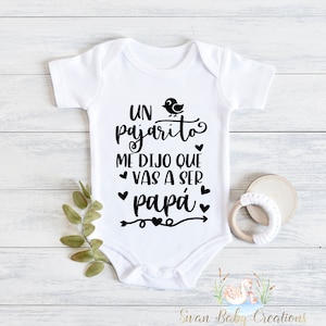May include: White baby onesie with black text that reads "Un pajarito me dijo que vas a ser papá" with a small bird illustration and hearts.